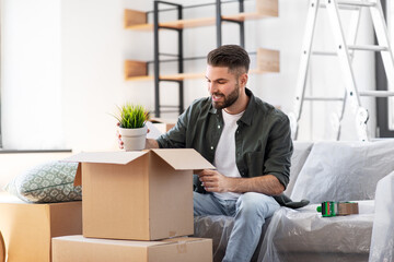moving, people and real estate concept - happy smiling man with boxes and flower at new home