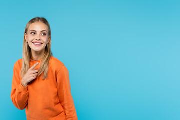 Smiling blonde woman pointing with finger isolated on blue