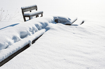 Wooden pier and bench covered with snow