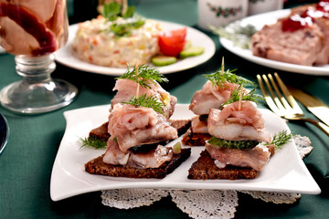 White plate with mini canapes with herrings for Christmas on festive table