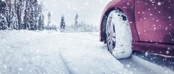 Panoramic view of the red car on the snowy road in snowfall.