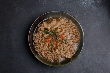 Instant noodles in gray Japanese ceramic lining with black tray, top view.