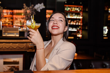 happy young woman drinks a cocktail at a bar counter