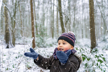 Fototapeta na wymiar Close up portrait of a little boy playing with snowflakes in a park in winter. Happy child enjoys the first snow in a forest. Waiting for Christmas.