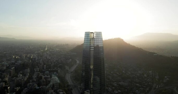 Aerial orbit of the city of santiago de chile with its island hills in the background and a sun ray on the side.