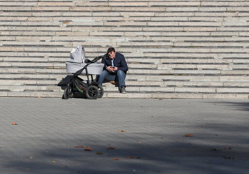 A man uses his mobile phone near a baby carriage on a sunny autumn day in central Chisinau