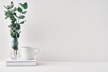 A mug, a stack of books, a wooden board and a transparent vase with eucalyptus branches. Eco-friendly materials in interior decor, minimalism. Copy space, mock up