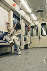 A girl in a beige trench coat rides in a subway car