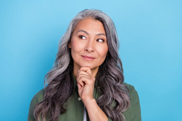 Photo of charming thoughtful retired woman wear green shirt arm chin looking empty space smiling isolated blue color background