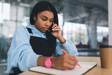 Obraz premium Black girl writing and talking on smartphone