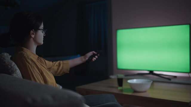 teen girl is sitting on the sofa at home in the evening watching tv and switching channels, chroma key, cinematic shot