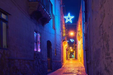 Authentic tiny street of old city Malta in the Christmas decor and illuminations, Christmas star and lights - obrazy, fototapety, plakaty