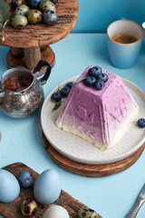 Traditional Easter Orthodox curd cake with blueberry. Traditional Easter cottage cheese dessert. Flowers, blueberry, eggs. Blue background, side view