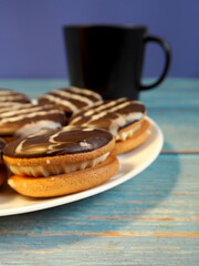 a white plate with chocolate cookies stands on a blue wooden table next to a mug of natural coffee. side view. breakfast