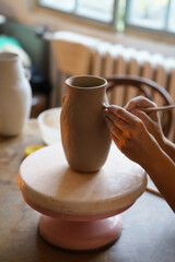 Craftsmanship hobby concept: hands of professional ceramist working on pottery vase in studio. Cropped image of potter master creating jug of raw wet clay during classes in workshop creative space