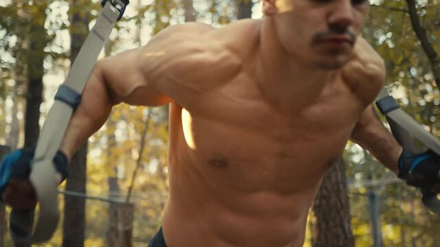 Close up of sporty man doing exercise for hands and for all body with trx fitness straps. Working hard. 