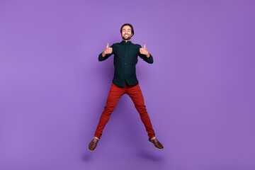 Fototapeta na wymiar Photo of cute funky young man wear smart casual outfit smiling jumping showing thumbs up isolated purple color background