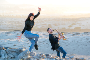 latin musician is playing saxophone while latin woman is dancing in the desert landscape