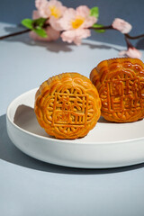 Chinese traditional pastry Moon cake, Mooncake, The Chinese character on the cake translation in English is"lotus paste", Mid-Autumn Festival, harsh sun light, blue background, modern still life