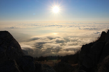 View from the top at sunrise in the mountains. sun disk on the horizon above the clouds