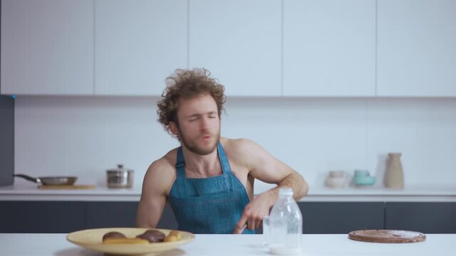 Masturbation concept. Glaze preparation. Whipped cream. Young handsome curly guy cooking in kitchen. He is wearing a blue apron. High quality 4k footage