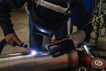 Welder is welding the steel in the factory. Weld the steel in dark. Workers wearing industrial uniforms and welding masks at a welding factory protect from welding sparks. Occupational safety concept