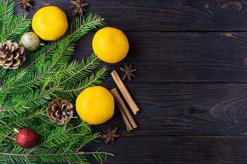 Orange ripe tangerines on a dark wooden table. Green fir branches with Christmas decorations in the background. Top view, space for text