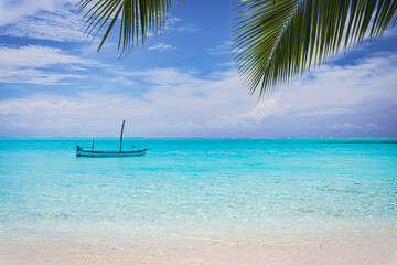 Old fishing boat on a paradise island with turquoise water and palm leaves in the foreground - Maldives