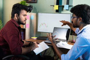 Traders analysing by discussing about stock market charts while working at office - concept of...