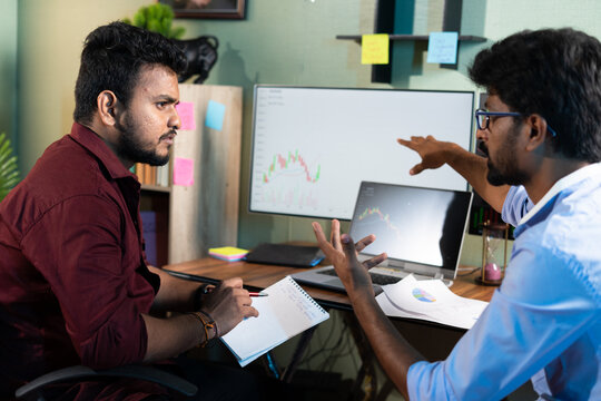 Traders analysing by discussing about stock market charts while working at office - concept of teamwork, learning or planning share market strategy and financial investment.