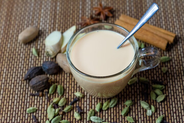 Masala chai tea in transparent glass cup with ginger, cardamom, cinnamon, nutmeg, and anise on bamboo mat background. Masala chai popular traditional India hot drink made of milk, tea and spices.