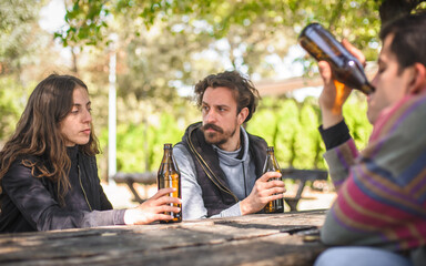 Unhappy young friends drinks beer from bottle on wooden bench