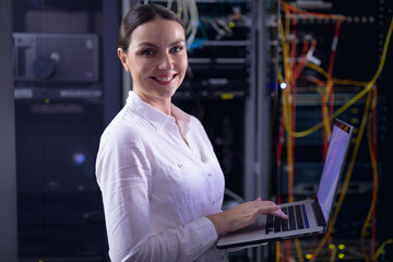 Fototapeta na wymiar Portrait of caucasian female engineer smiling while using laptop in computer server room