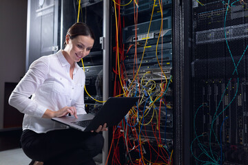 Caucasian female engineer using laptop and inspecting computer server in computer server room