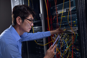 Fototapeta na wymiar Asian male engineer using digital tablet and inspecting computer server in computer server room