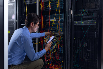 Asian male engineer using digital tablet and inspecting computer server in computer server room