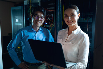 Fototapeta na wymiar Portrait of diverse male and female engineers with laptop smiling in computer server room