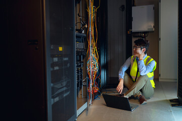 Asian male engineer wearing high visibility vest with laptop inspecting in computer server room