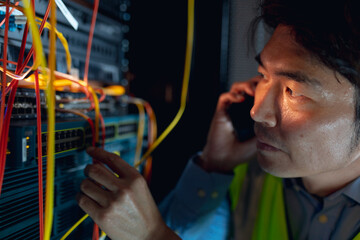 Close up of asian male engineer talking on smartphone while inspecting in computer server room