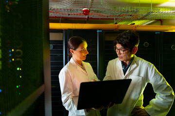 Diverse male and female engineers wearing aprons using laptop while inspecting in server room
