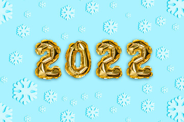 Obraz na płótnie Canvas 2022 golden foil balloons with snow decor and Christmas snow with copy space on blue background. New Year and Xmas concept