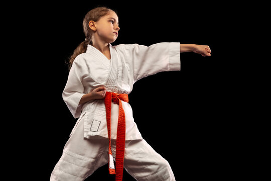 One little girl, young karate in kimono practicing isolated over dark background. Concept of sport, education, skills
