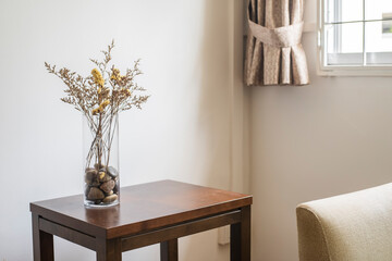 Stylish modern dried flower arrangement in a glass vase with pebbles in it on a brown wooden table,...