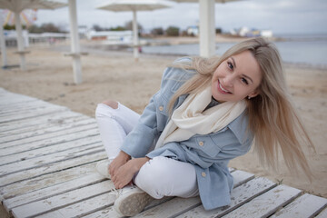 Fototapeta na wymiar Beautiful woman dressed woolen blue jacket, white scarf and trousers walking in the beach, reston and enjoy the time is in with you, against the shore of the beach at background sea and sky
