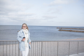 Beautiful woman dressed woolen blue jacket, white scarf and trousers walking in the beach, reston and enjoy the time is in with you, against the shore of the beach at background sea and sky