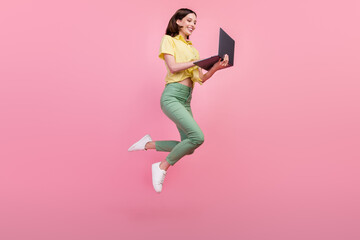 Full size profile side photo of young girl happy smile jump chat type laptop email isolated over pink color background