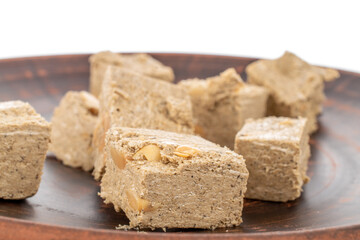 Several pieces of halva with peanuts on a clay dish, close-up, isolated on white.