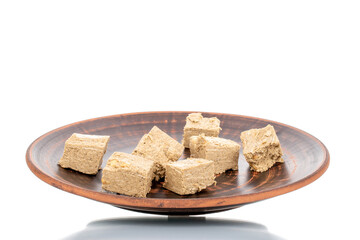 Several pieces of halva with peanuts on a clay dish, close-up, isolated on white.
