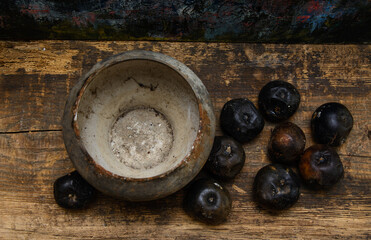 An old cast iron pot stands on a wooden board. Black rotten apples lie nearby. View from above