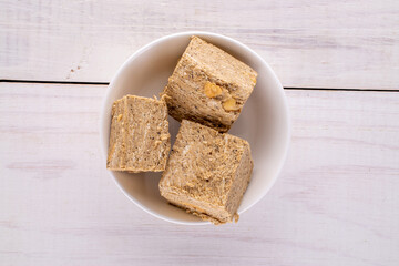 Three pieces of halva with peanuts with a white saucer on a wooden table, close-up, top view.
